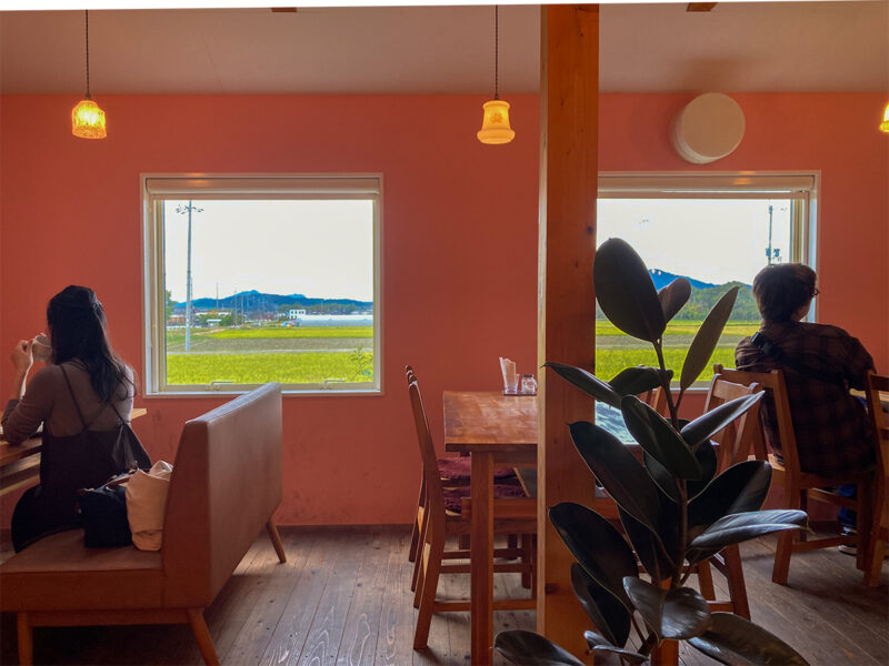 ピンク色の壁に囲まれた「sweets & Café MILK」のテーブル席。窓からはのどかな田園風景が広がります
